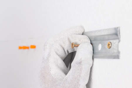 close-up of the builder's hand, in the process of fixing a metal plate, for fixing hanging furniture
