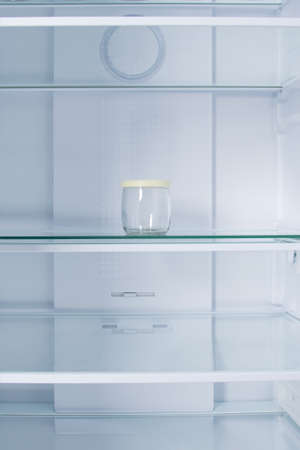 against the background of a white refrigerator, on a shelf, there is a small glass jar with a plastic lidの写真素材