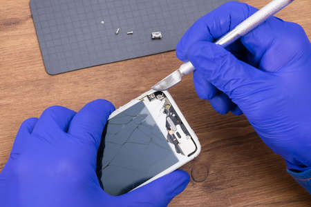 close-up of a smartphone screen repair, on a wooden background, fragments are removed from the case with a scalpelの写真素材