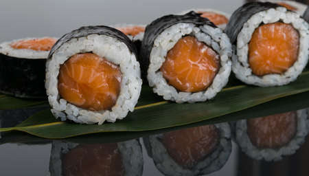 on a dark table with a reflection, close-up, salmon rolls, on a bamboo leafの写真素材