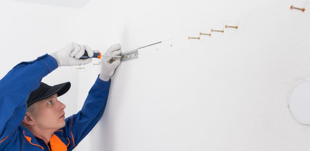 a worker in a blue uniform, on the background of a white wall, we fasten the bracket for hanging furnitureの写真素材