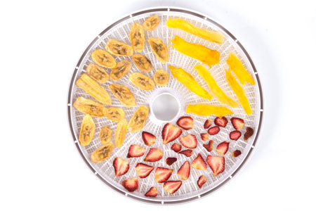 electric dryer for fruits and vegetables, close-up, strawberries, banana and mango are laid out on a round grate, on a white backgroundの写真素材