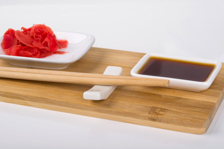 close-up, on a white background, on a wooden board, sticks for Japanese sushi and containers with soy sauce and pickled gingerの写真素材