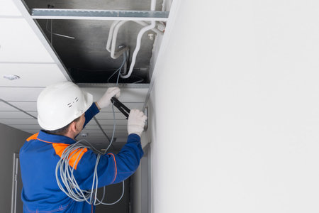 a master in a blue uniform and a white helmet, laying wiring for a WiFi router in a hidden false ceiling system, there is a place for an inscriptionの写真素材