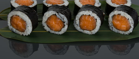 on a black table with a reflection, on a bamboo leaf, Japanese salmon rolls are laid out in a rowの写真素材