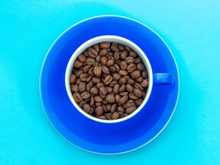 Cup full of coffee beans isolated on blue backgroundの写真素材