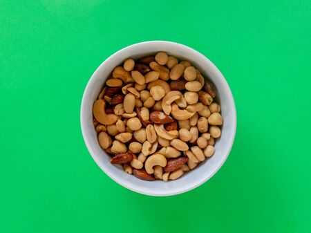 A bowl of a roasted nut mix isolated on a green backgroundの写真素材