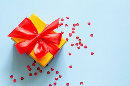 Yellow closed gift box with party confetti on a blue background on the left side. Flat layの写真素材