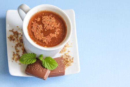 Milk chocolate Milka with a fresh mint leaf and a cup of hot cacao.