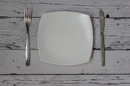 Empty plate, fork and knife over wooden background. Clean plate and cutlery on light background. Top...