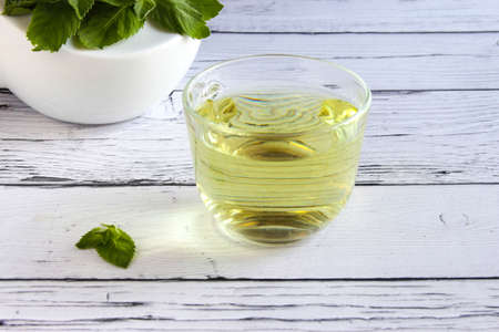 Fresh mint tea concept on a wooden background. Mint tea in a transparent cup and one mint leaf on...