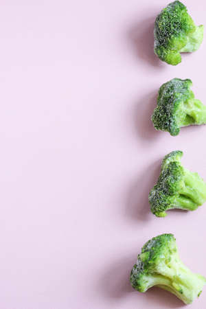 Frozen vegetables such as broccoli cabbage laid out on the right side on a pink background. Copy space. Top view. Vertical orientation.の写真素材