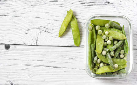 Frozen vegetables such as green pods and peas in the transparent bowls on the wooden background with copyspace. Top view.