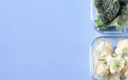 Frozen vegetables such as cauliflower and broccoli cabbage in the transparent bowls on the concrete blue background. Copy space, top viewの写真素材