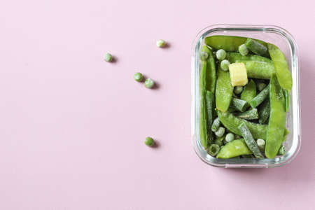 Frozen vegetables such as green pods and peas in the transparent bowls on the pink background with copyspace. Top view.の写真素材