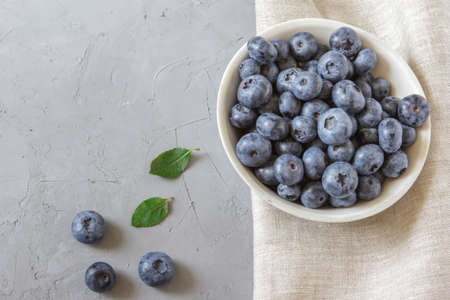 Fresh blueberries in white bowl. Fresh blueberries with green leaves on gray table. Concept for healthy eating and nutrition. Top view. Copy space.の写真素材