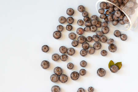 Fresh blueberries spilled out of the transparent bowl. Fresh blueberries on blue table. Concept for...
