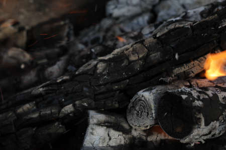 Smoldered logs burned in vivid fire close up. Atmospheric background with flame of campfire. Unimaginable detailed image of bonfire from inside with copy space. Whirlwind of smoke and glowing embers.の写真素材