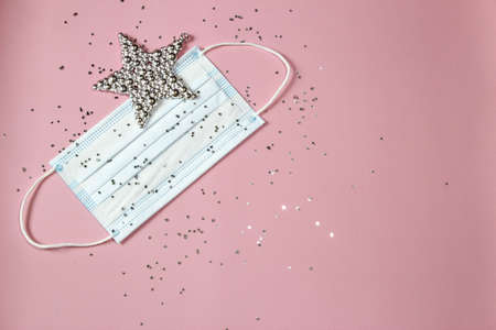 Hygienic face mask with confetti and silver star on a pink background. Christmas and New Year 2021...
