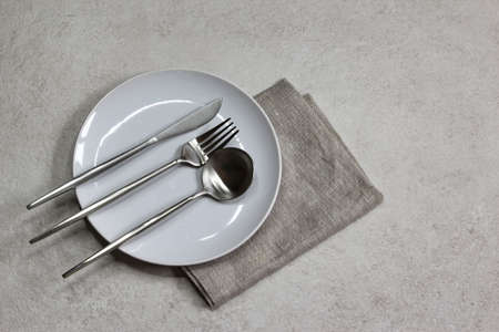 White empty plate with knife, spoons and fork gray textile napkin on grey stone background. Table setting. Top view.の写真素材