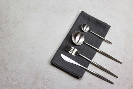 Knife, spoons and fork with dark textile napkin on grey stone background. Table setting. Top view.の写真素材