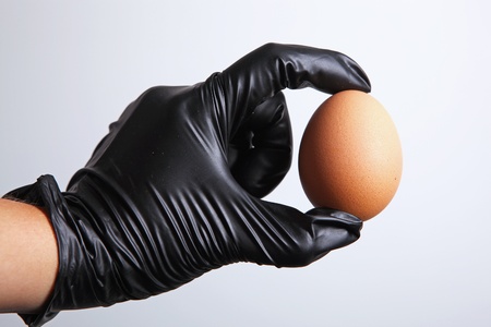 A hand in a black latex glove holding an egg