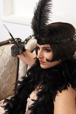 A beautiful young girl dressed in the style of 1920's, sit in the armchair and hold cigarette...