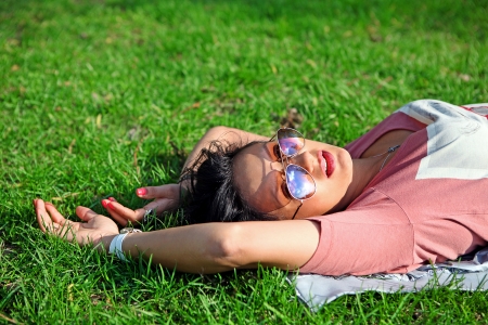 A pretty young dark-haired girl in sunglasses lying on the grass の写真素材