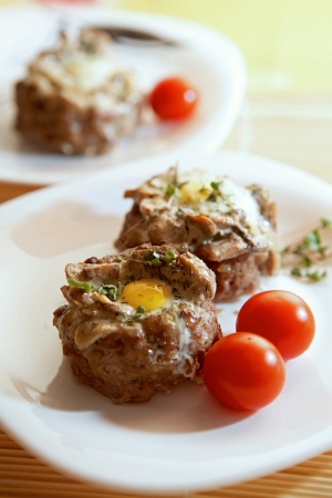 Delicious quail eggs in the minced meat with mushrooms, decorated with cherry tomatoes and broccoli sprouts on white plates.の写真素材