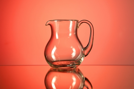 A glass creamer with a reflection on a red background.の写真素材