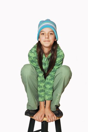 An very young teen girl is sitting on an bar chair in her green clothing like a frog. の写真素材