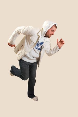A young athletic man posing running in the studio with an white jacket and the hood over his head, on beige background.の写真素材
