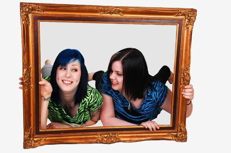 Two young girls laying on the floor and looking trough a picture frame over white background.