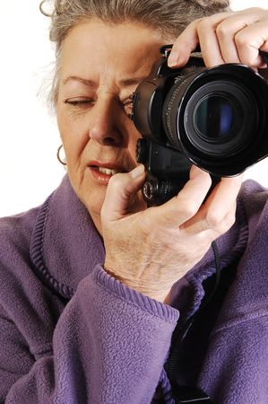 Senior woman with gray hair and a lilac home suit holds a digital camera and takes pictures of her...