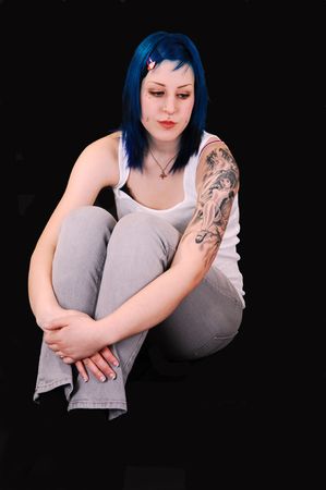 A very sad looking young girl with blue hair and a big tattoo on her lefty arm, sitting on the floor for black background, and the arms grossed around  the legs.の写真素材
