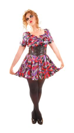 Beautiful red haired woman in a colorful dress with a big belt, black pantyhose and high heels standing in the studio wit her hands on the hips.の写真素材