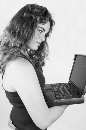A black and white photo of an young woman holding an laptop in her hand and is concentrated on the screen, with long curly hair.の写真素材