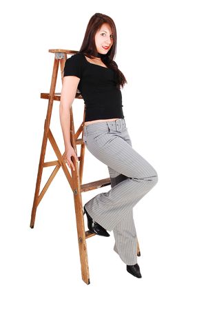 An young woman sitting on the step of a stepladder in a gray dress pants and black sweater, shooing her fantastic body.の写真素材