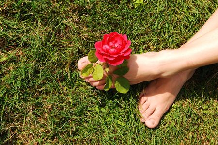 The feet of a young woman, sitting on the grass with a red rose between  her toes.の写真素材
