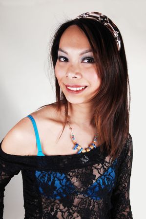 A portrait of a young Asian woman with long brunette hair an blue bra and an lace black blouse, with an headband smiling, on light gray background.の写真素材