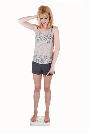 A young woman is very sad, standing on a scale and find out she gains some wait, in shorts and a lace top on white background.の写真素材