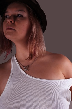 A young blond woman in an undershirt and a black hat on gray background.の写真素材