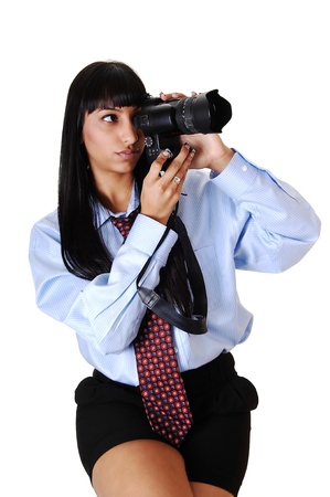 An pretty young woman with a dELS camera taking some pictures, in black shorts and a blue shirt and tie, sitting, over white background.の写真素材