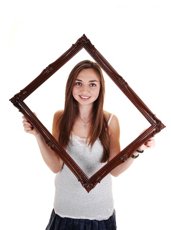 An beautiful teenager standing with an picture frame and gray t-shirt, with her long brunette hair, over white background.の写真素材