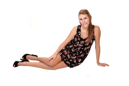 A young pretty teenager in a short black collared dress and long brunettehair sitting in high heels on the floor, for white background.の写真素材
