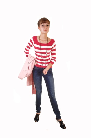A teenager standing with her pink coat over her arm in the studio, injeans and high heels, for white background.の写真素材