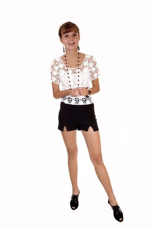 An lovely girl teenager in high heels, black shorts and white blousestanding in the studio with her slim body, for white background.の写真素材
