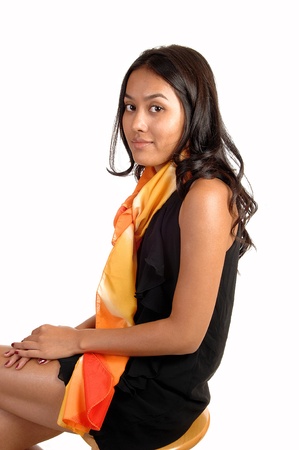 A pretty brunette haired Asian woman in a black dress, sitting on a chairwith a colorful scarf around her neck, for white background.の写真素材