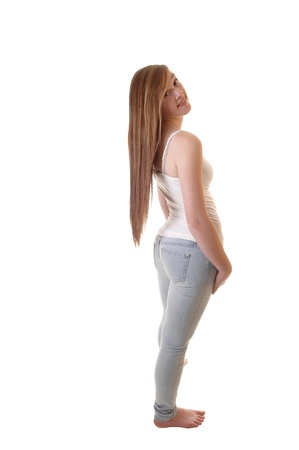 A young pretty teenager in jeans and white t-shirt standing bare feetinto the studio and her long brunette hair hanging down on her back.の写真素材