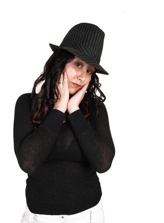 A young pretty girl in a black sweater and gray hat, holding her face in herhands with her long curly black hair looking sad into the camera.の写真素材